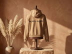 WOVYN Becoming Collection Hoodie - Soft Sand in a styled interior, back view with Sanskrit embroidery “यत् भावो – तत् भवति”