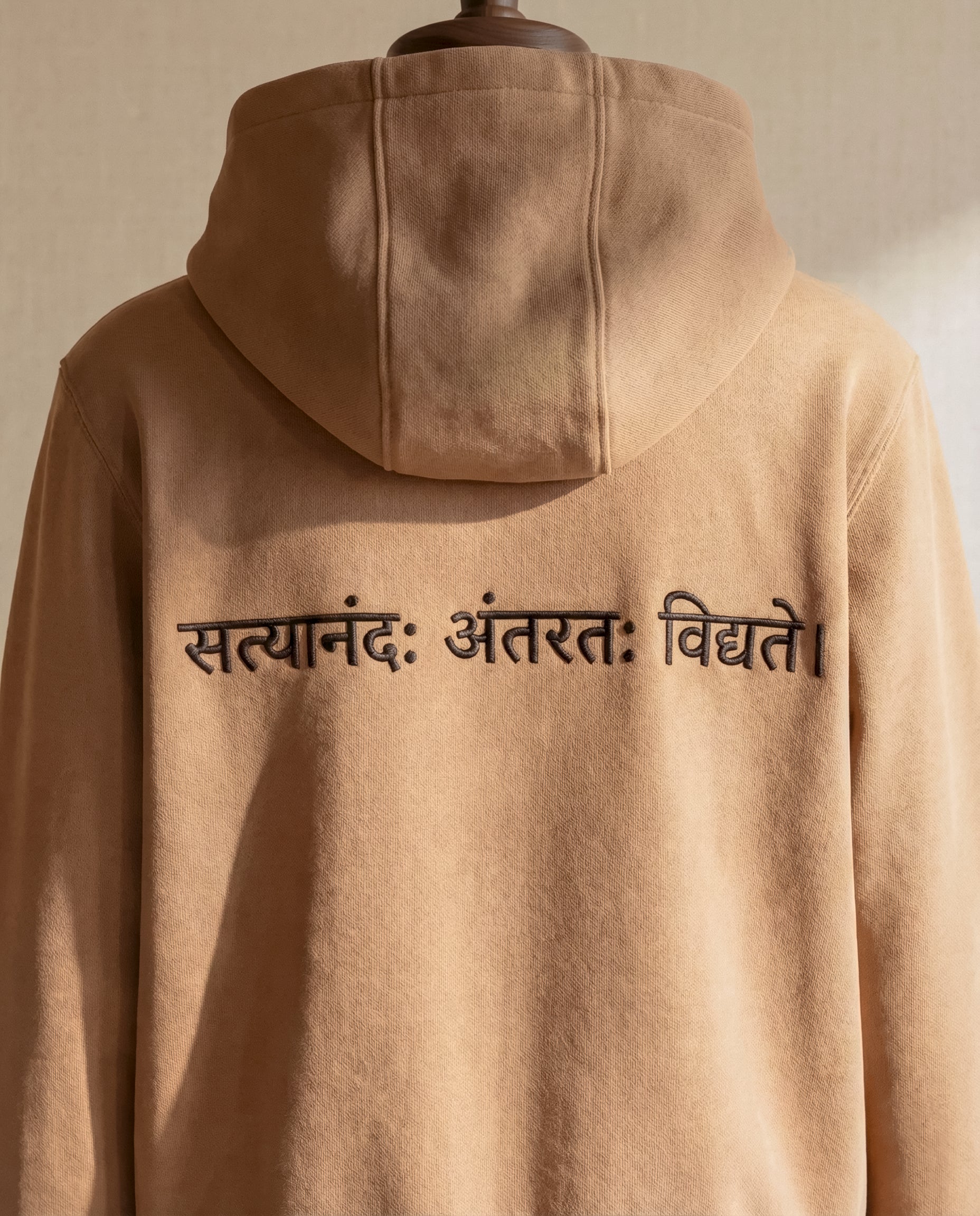 WOVYN Contentment Collection Hoodie - Soft Sand, close back view showing Sanskrit embroidery “सत्यानंदः अंतरतः विद्यते।” beneath the hood