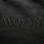 Macro detail of tonal WOVYN logo embroidery on the Obsidian Black hoodie, showing heavyweight fleece texture